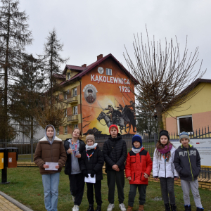 Grupa uczestników gry terenowej, stojąca w pobliżu przedszkola w Kąkolewnicy.