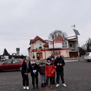 Grupa uczestników gry terenowej, stojąca w pobliżu lokalnego marketu "Zosia".