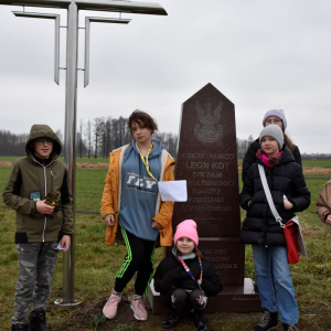 Grupa uczestników gry terenowej, stojąca przy pomniku upamiętniającym Leona Kota, bohatera Powstania Styczniowego.